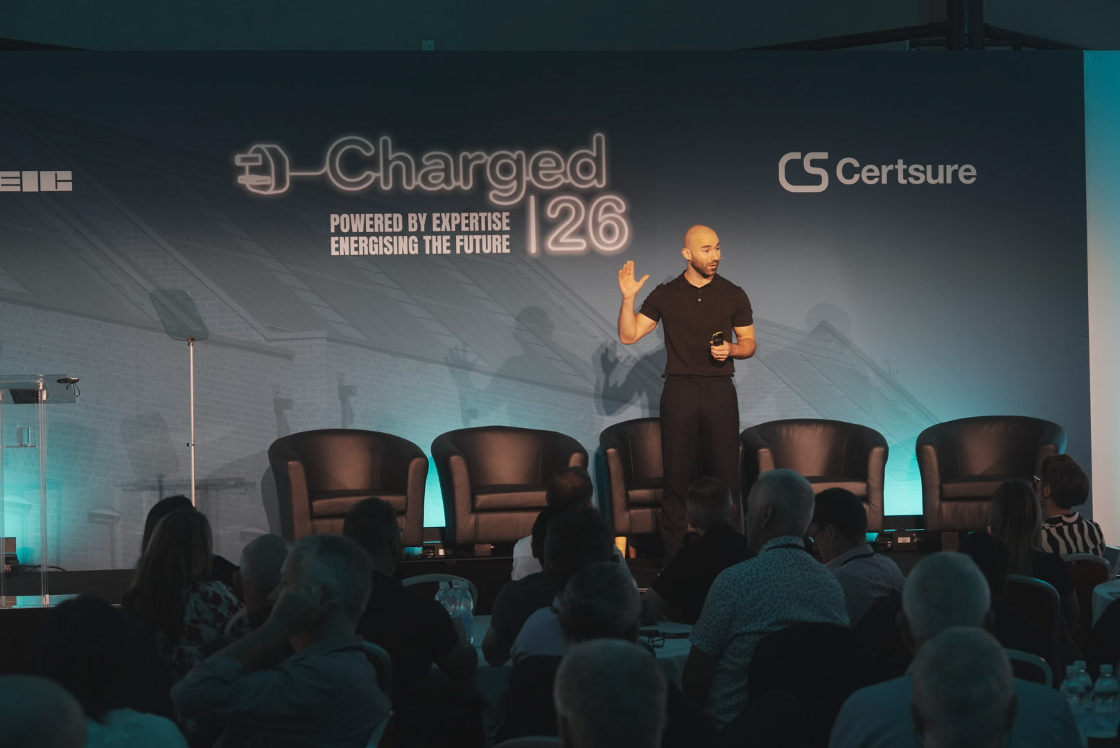 Speaker on the Charged 26 stage in front of the Certsure brand wall