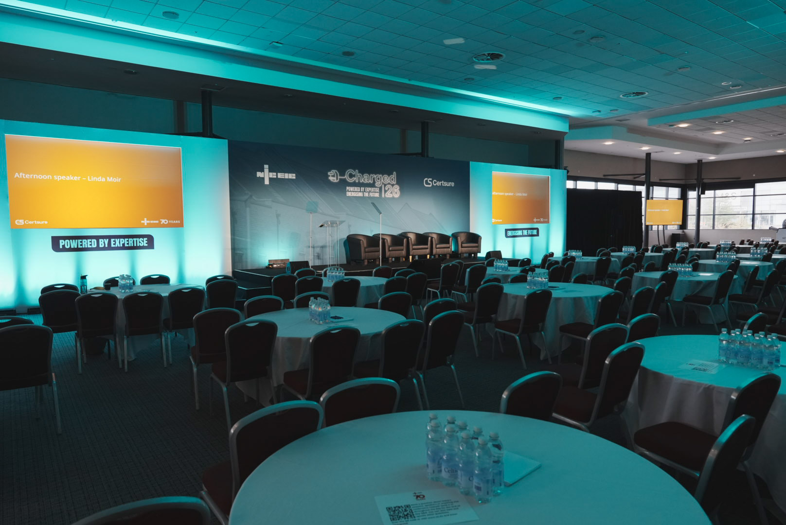 Charged 26 plenary room set with teal lighting and twin screens